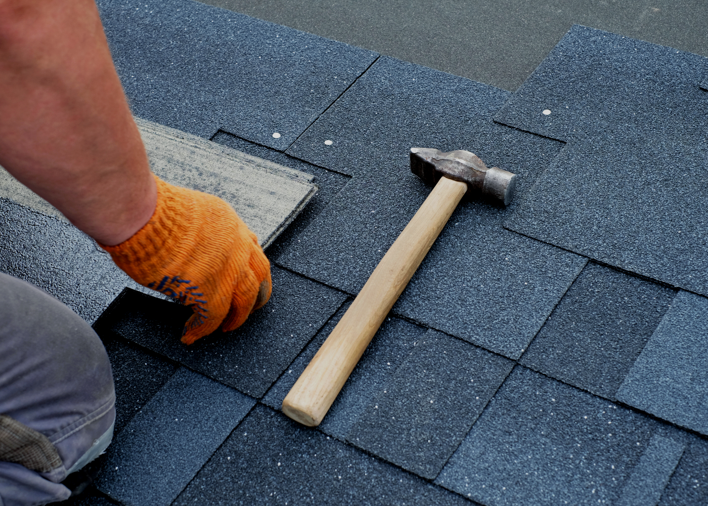 A person is installing shingles on a roof with a hammer.