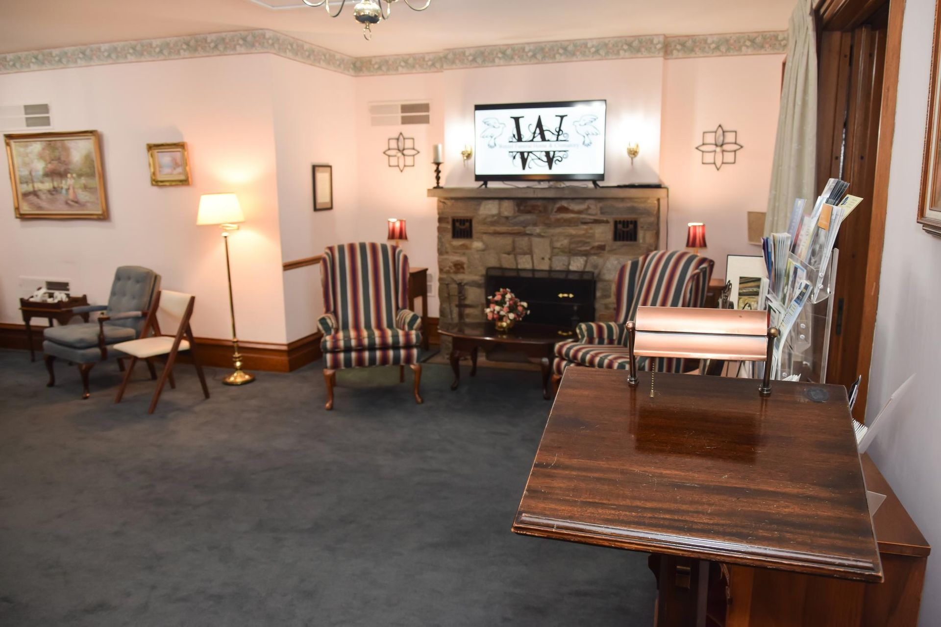 Living room with fireplace, striped chairs, TV, lamp, and dark carpet