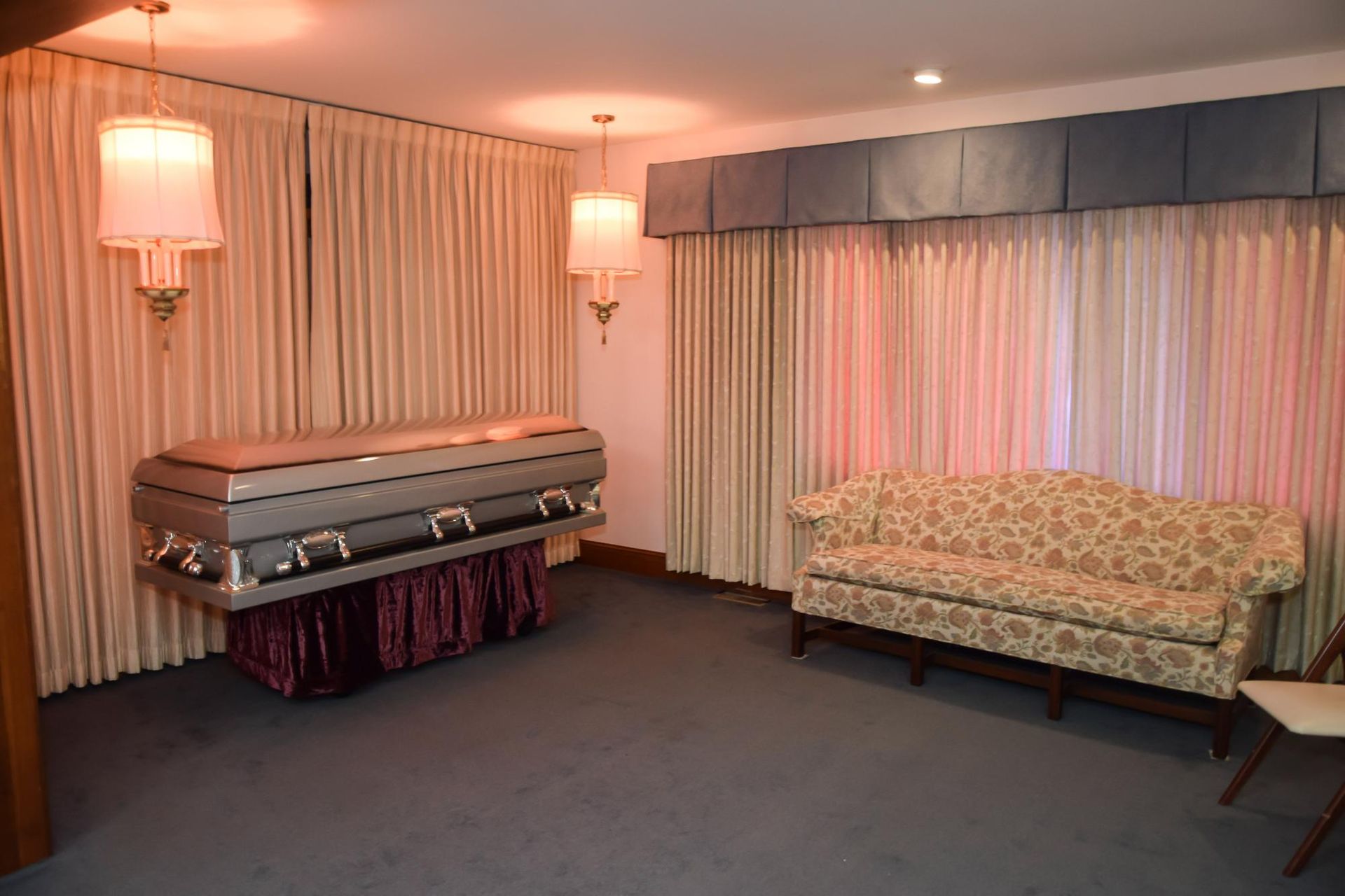 Funeral room with a casket, floral sofa, and soft pink lighting