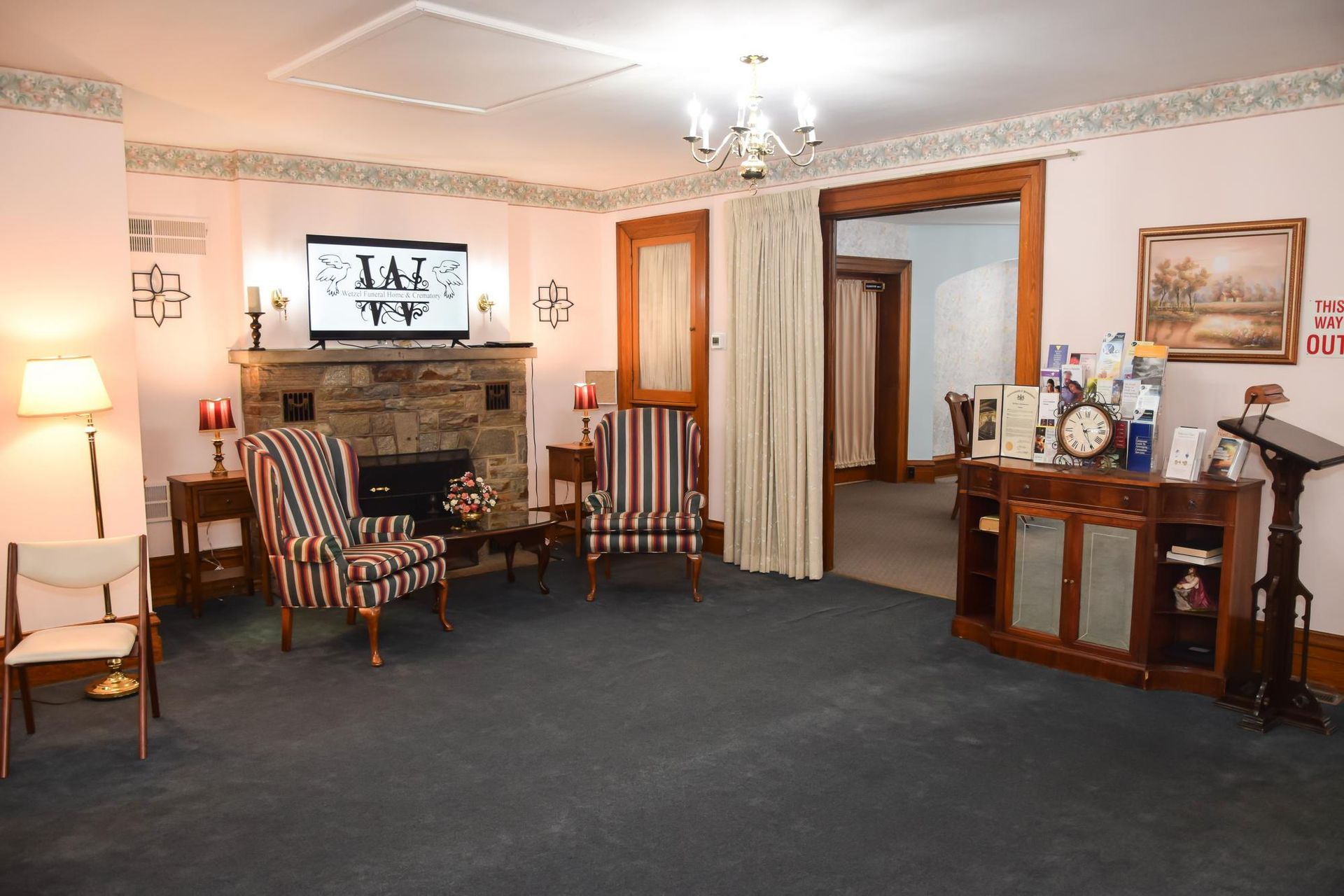 Cozy living room with fireplace, striped chairs, lamp, dark carpet, and wooden cabinet