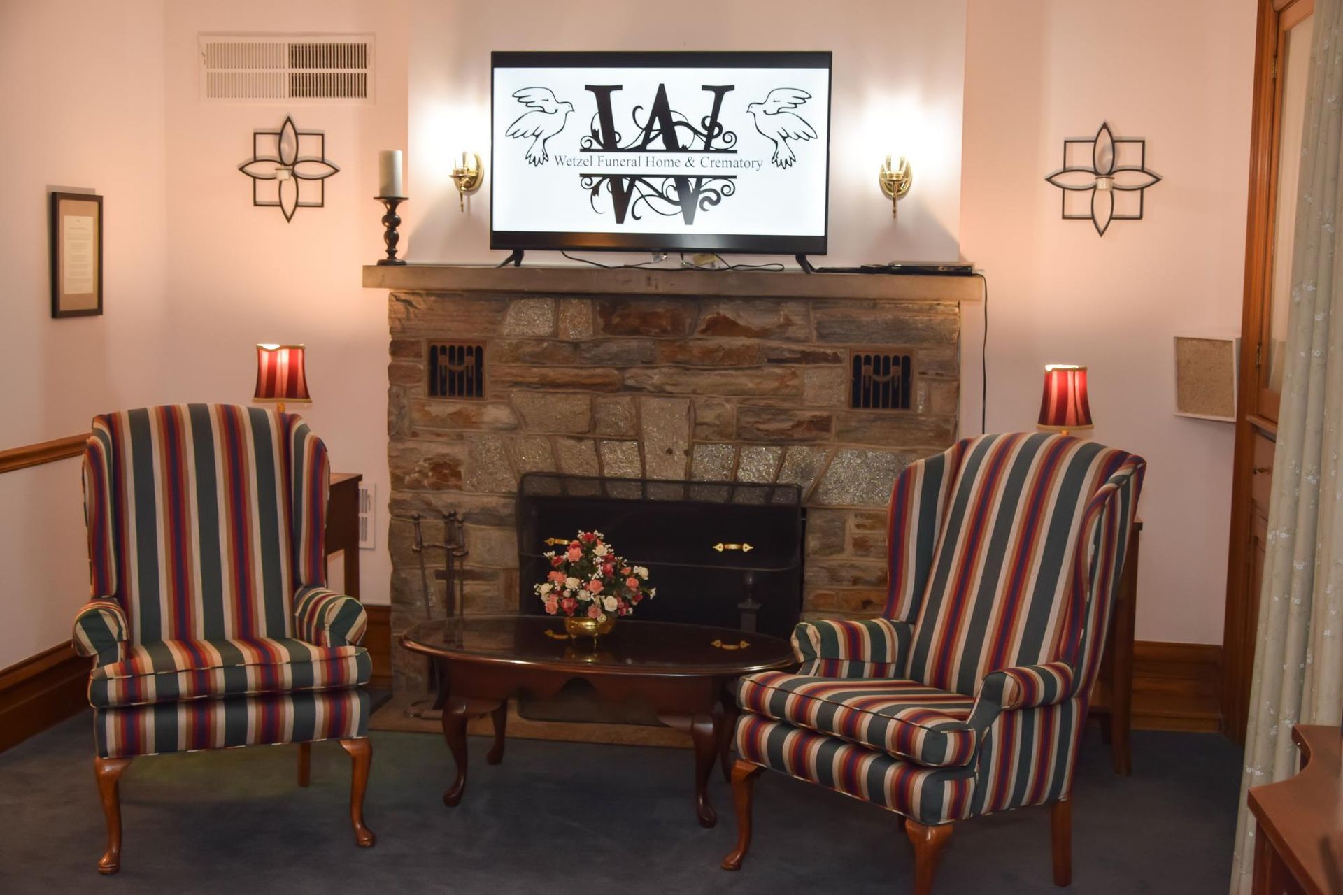 Cozy living room with a stone fireplace, striped armchairs, and a TV above the mantel.