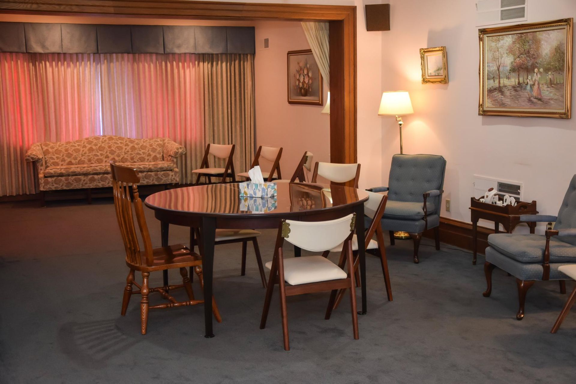 Cozy living room with a round dining table, chairs, blue armchair, lamps, and a curtained alcove bed area.