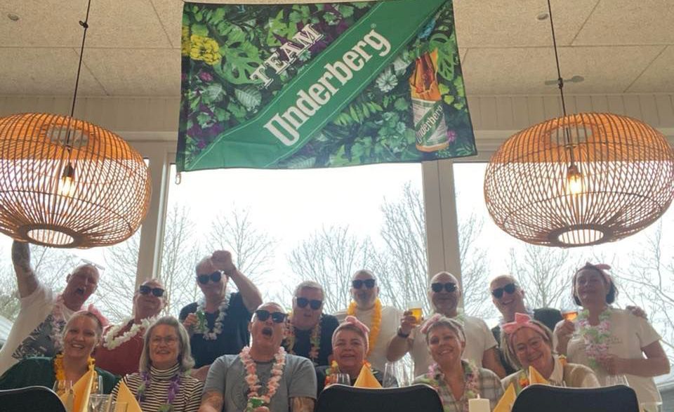 En gruppe mennesker stiller op til et billede under et banner, hvor der står team underberg