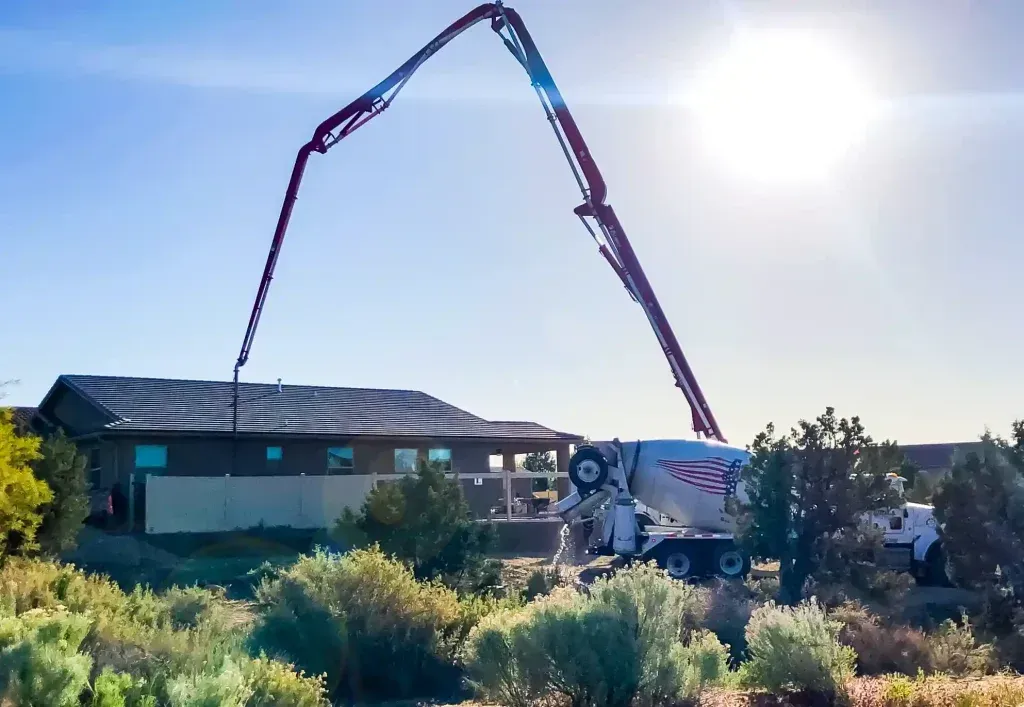 A concrete pump is pouring wet cement in front of a house.