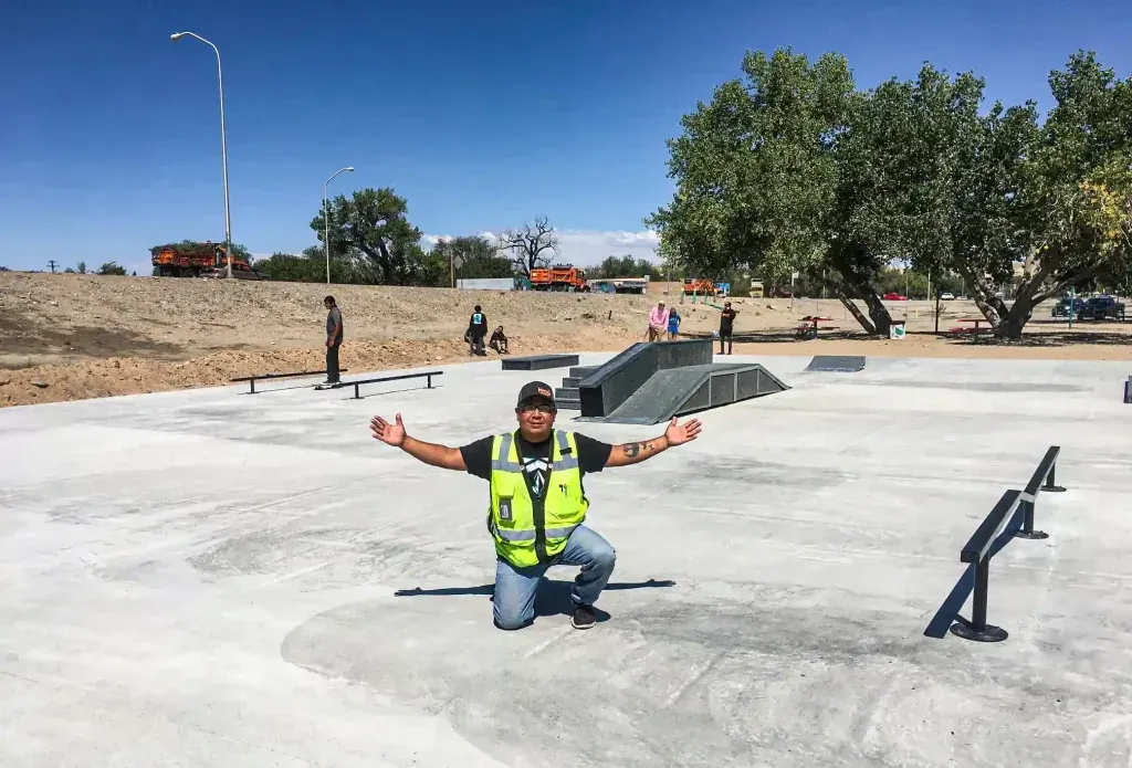 A man in a safety vest is kneeling on the ground in front of a skate park.