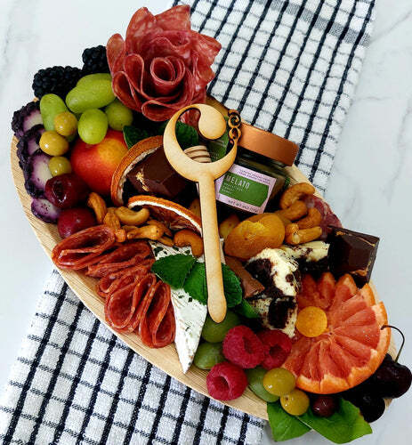 A wooden tray filled with fruits , nuts , and cheese on a table.