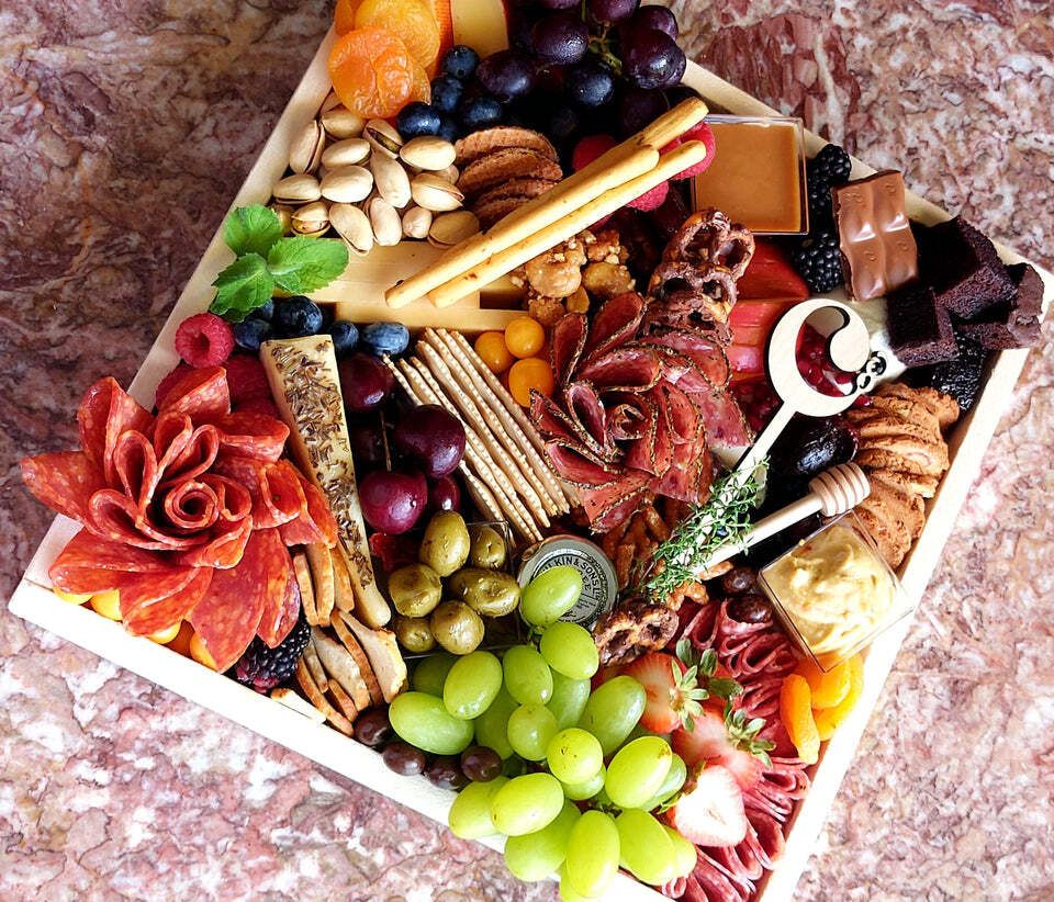 A wooden tray filled with fruits , nuts , cheese , and meat.