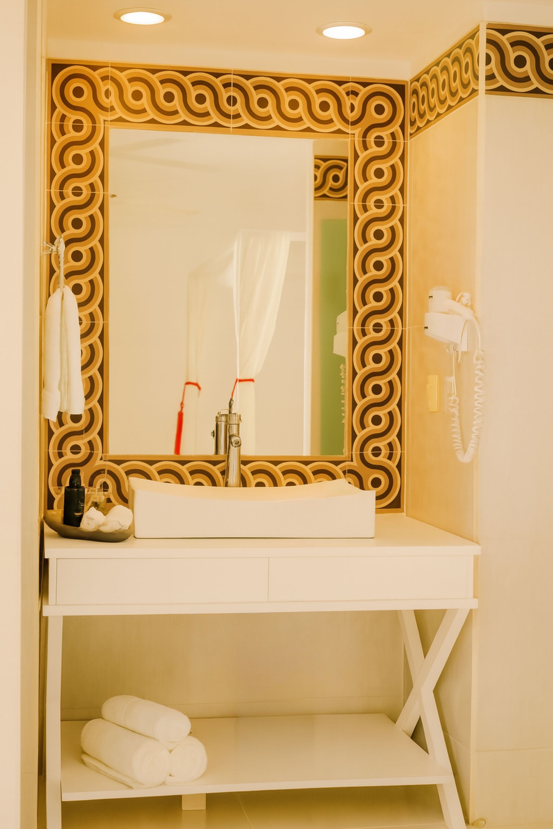 Bathroom with a white sink, mirror in a patterned frame, towels, and a hairdryer.