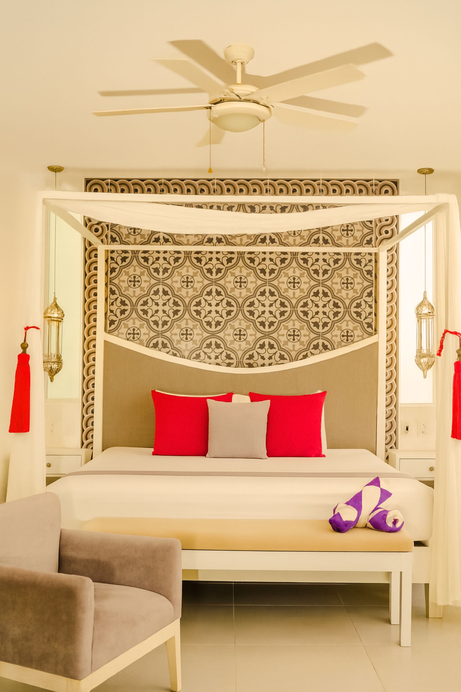 Bedroom with a canopy bed, decorative headboard, red pillows, bench, and armchair.