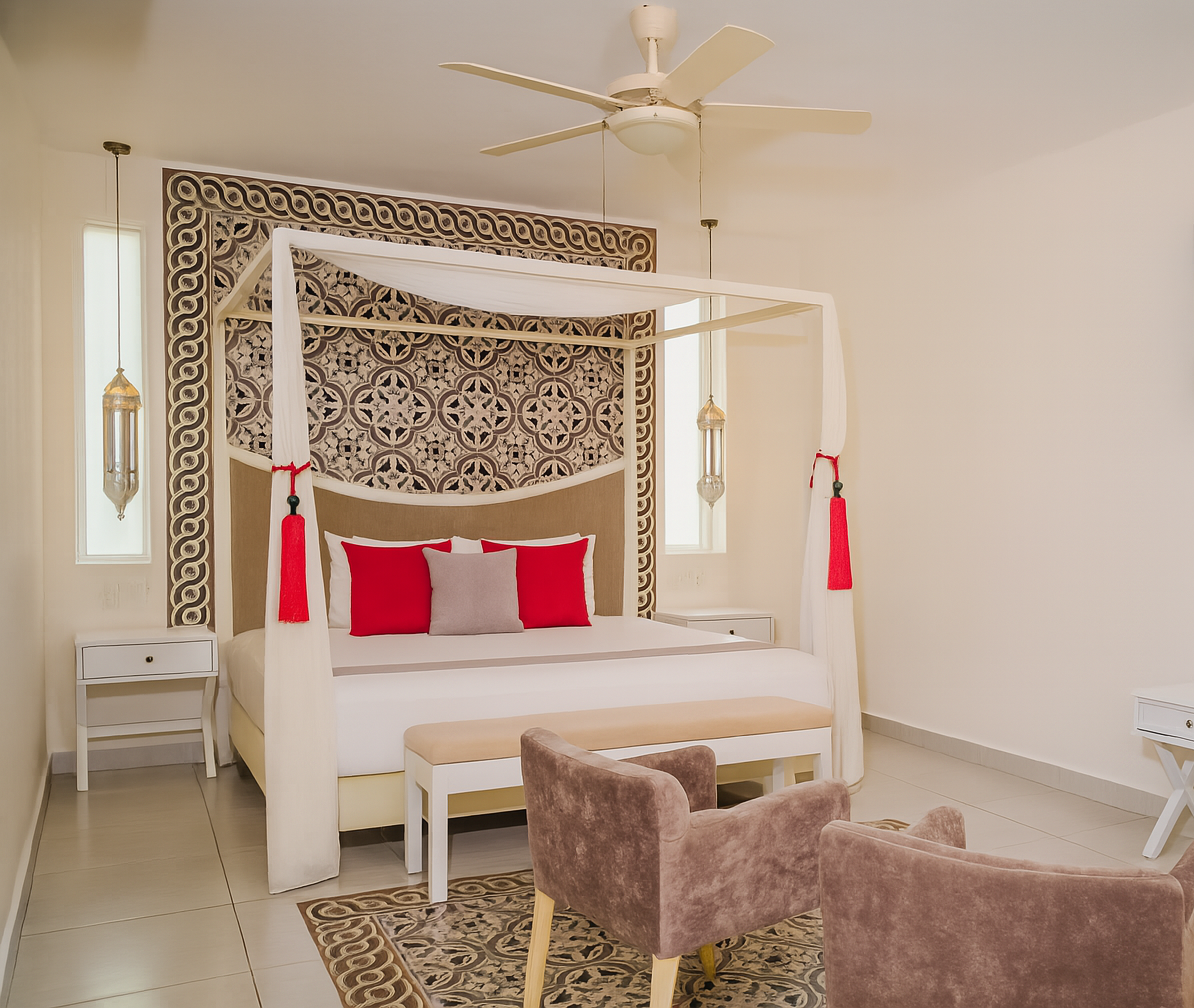 Bedroom with a four-poster bed, red pillows, patterned headboard, and two brown armchairs.