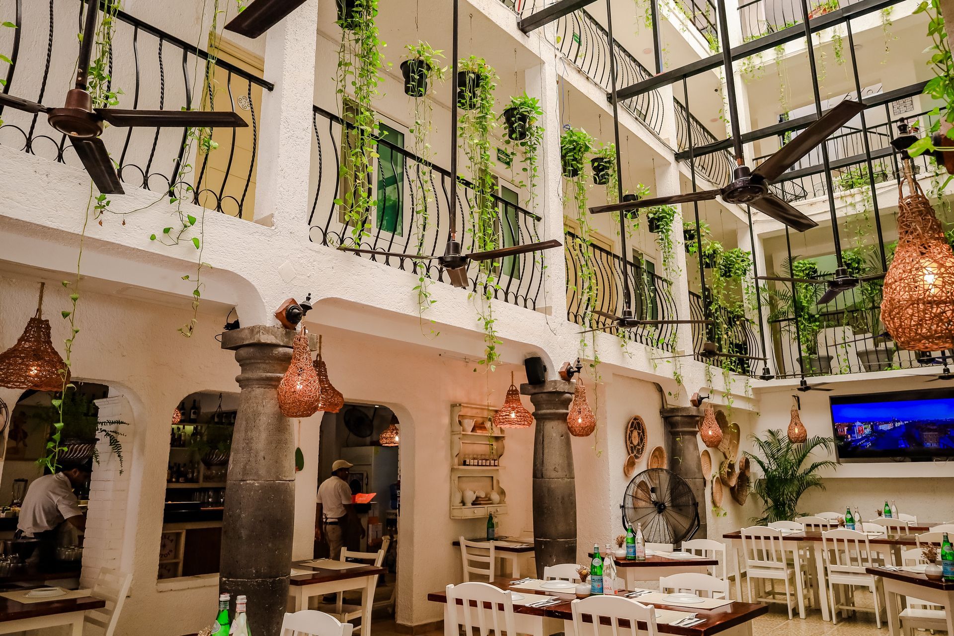 Restaurant interior with balconies, hanging plants, and white tables and chairs.