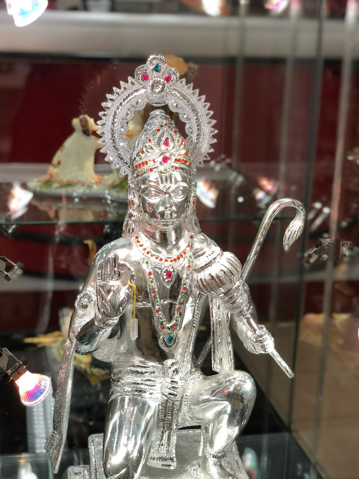 Op een glazen plank staat een zilveren beeld van een godheid.