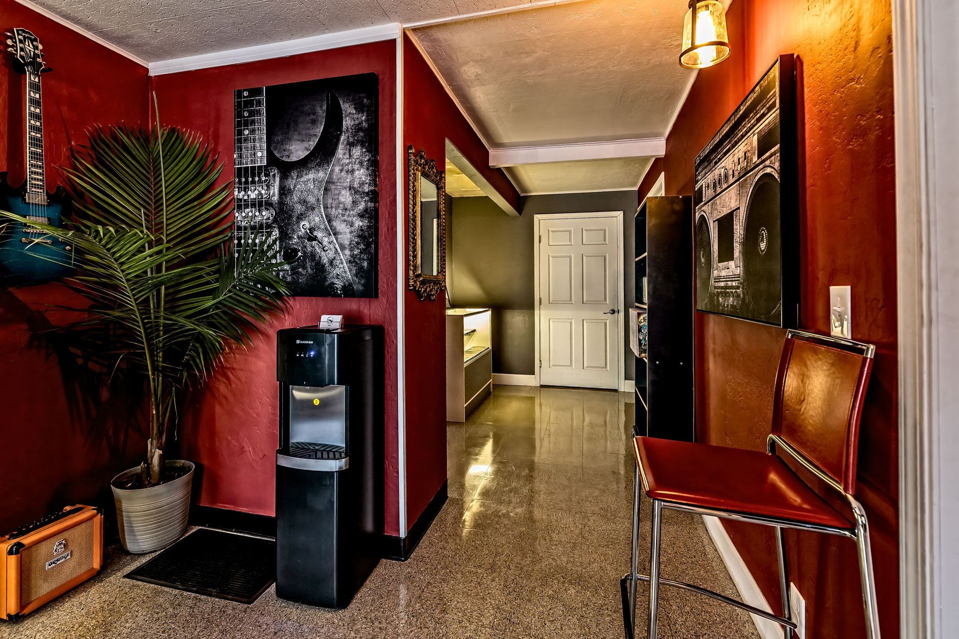 A hallway with red walls, a chair, a water dispenser and a guitar on the wall