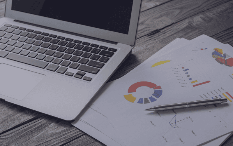 Una computadora portátil está sobre una mesa de madera al lado de un bolígrafo y papeles.