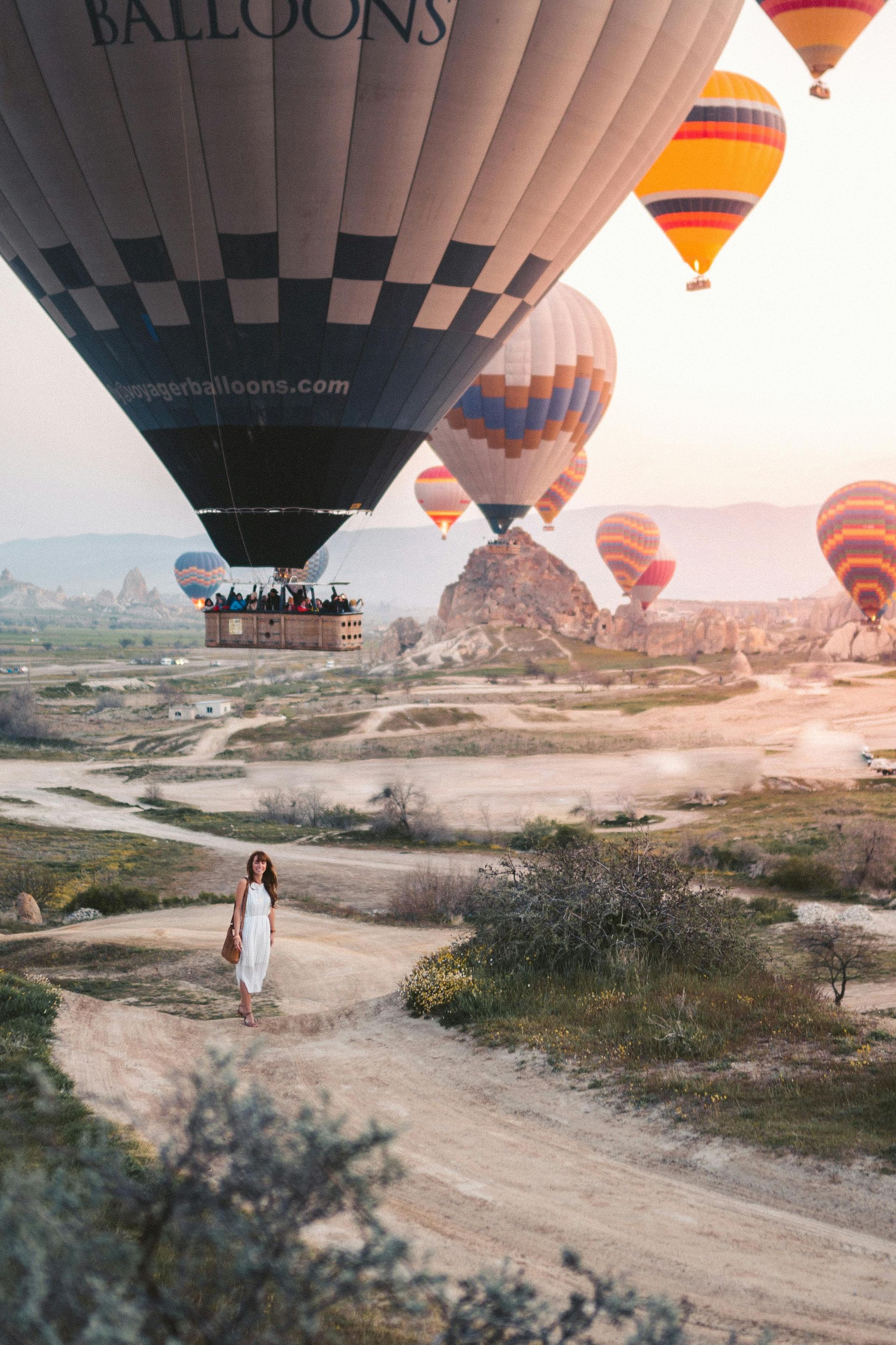 Una mujer camina por un camino de tierra frente a un campo de globos aerostáticos.