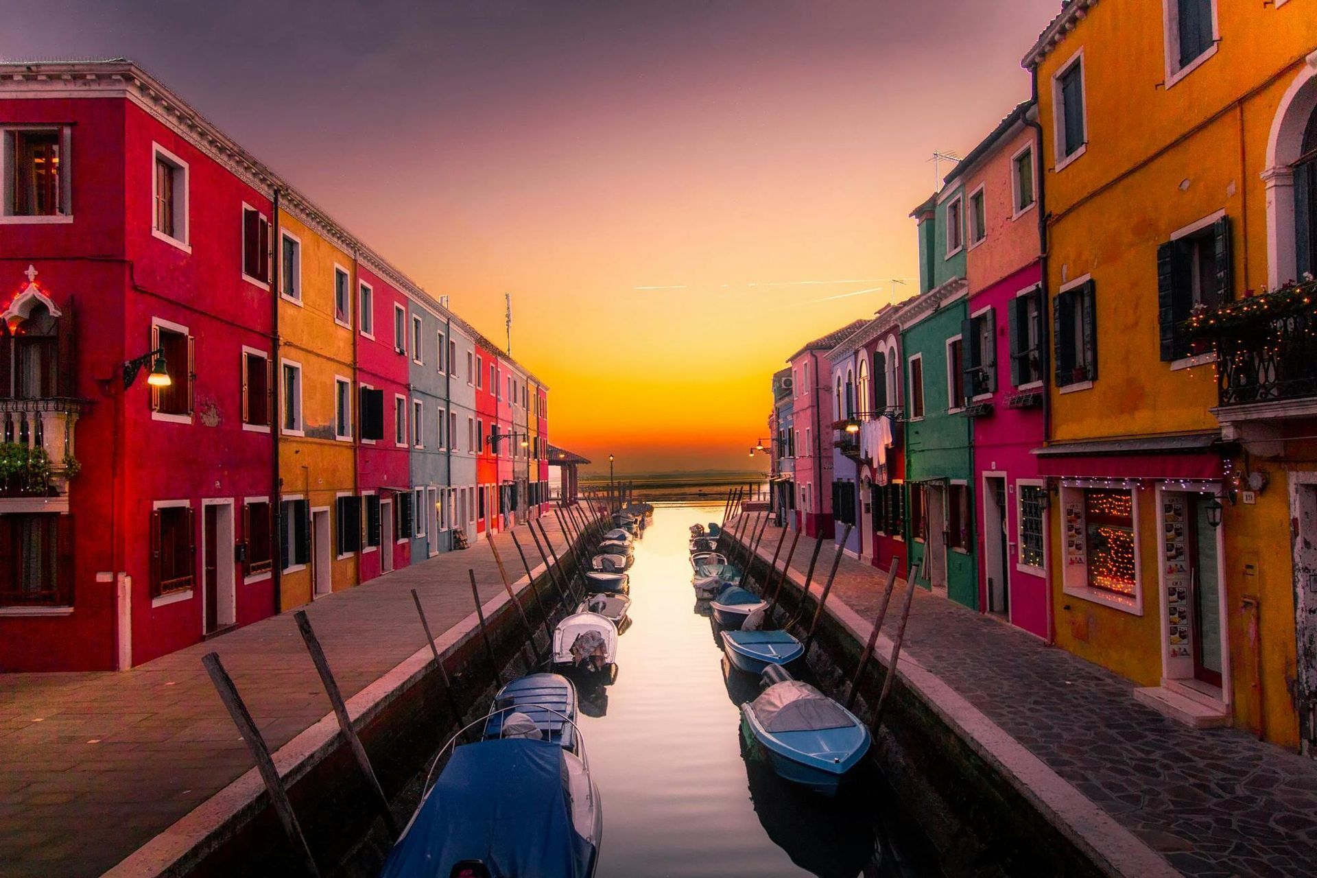 Una hilera de edificios coloridos a lo largo de un canal con barcos en el agua al atardecer.