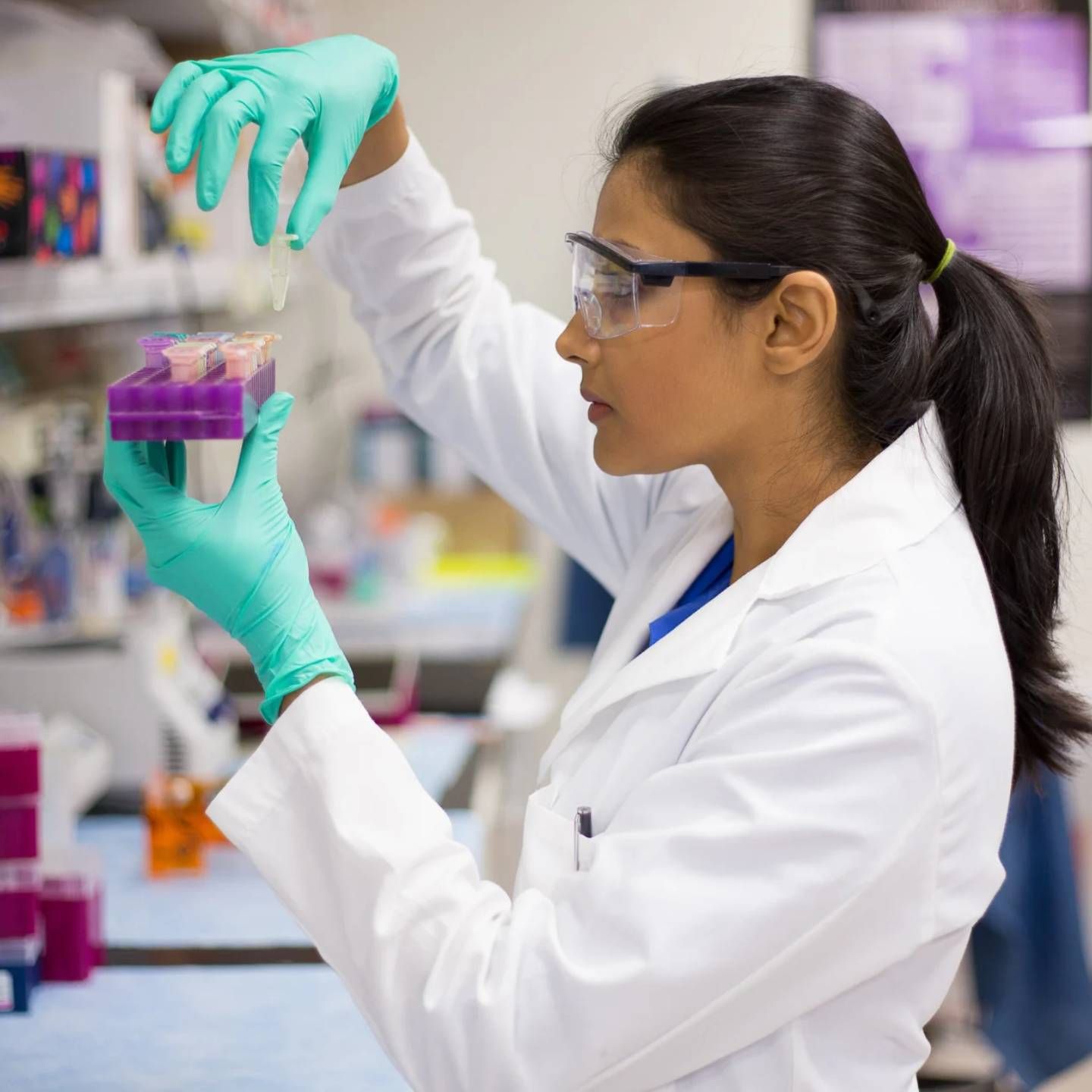 A woman in a lab coat and green gloves is holding a purple object.