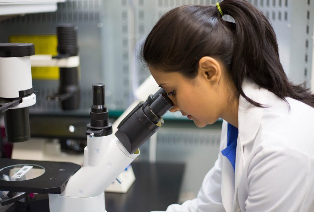 A woman is looking through a microscope in a laboratory.
