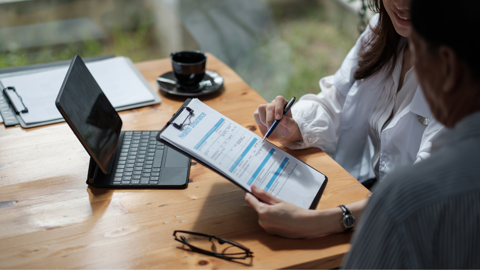 A man and a woman are sitting at a table looking at a clipboard.