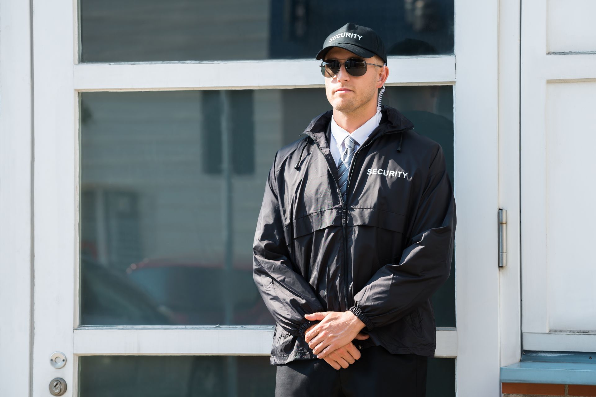 Man in black jacket and cap stands outside a white building with glass doors. Man in black jacket and cap stands outside a white building with glass doors.