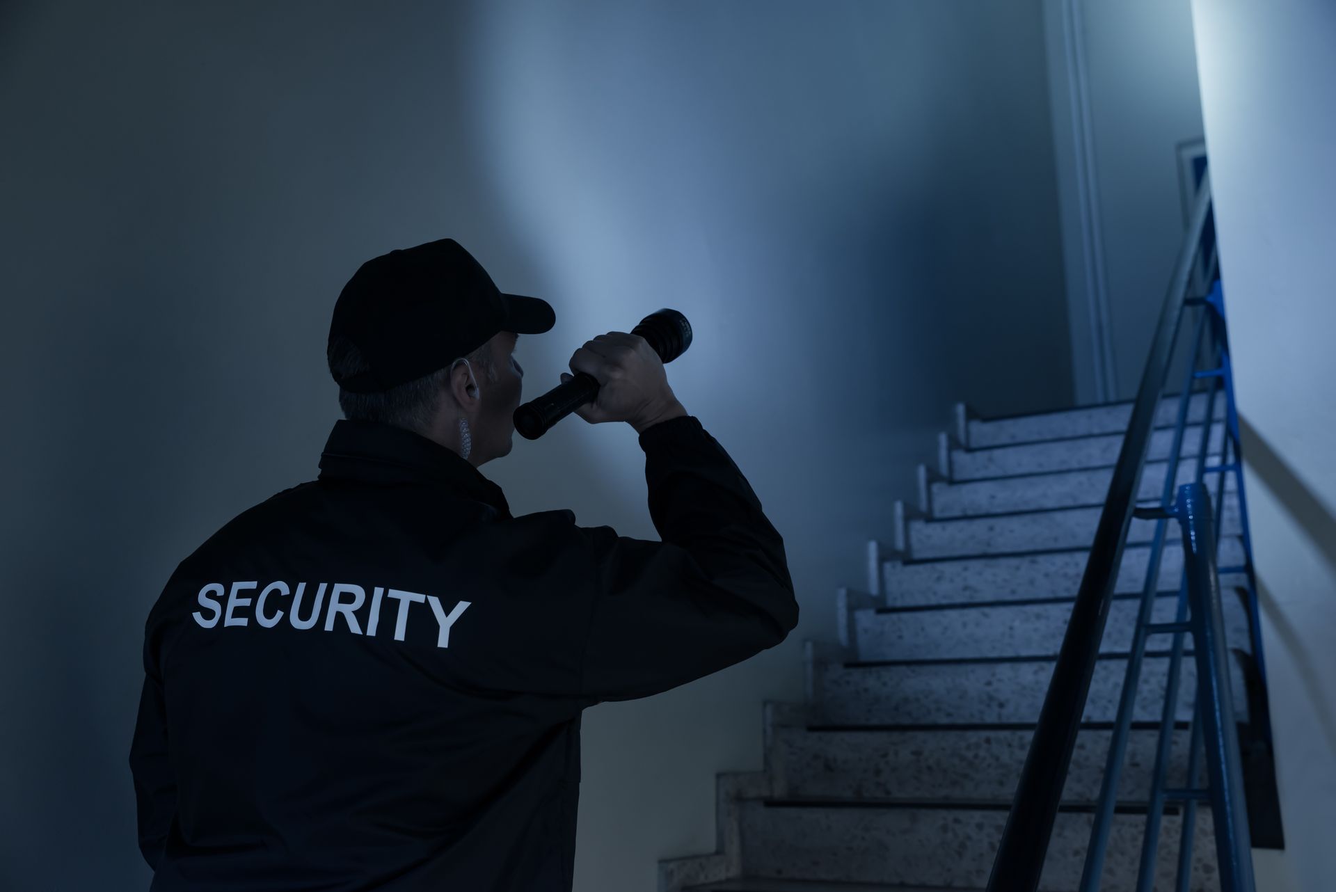 Security guard shining a flashlight up a stairwell in a dim blue hallway Security guard shining a flashlight up a stairwell in a dim blue hallway