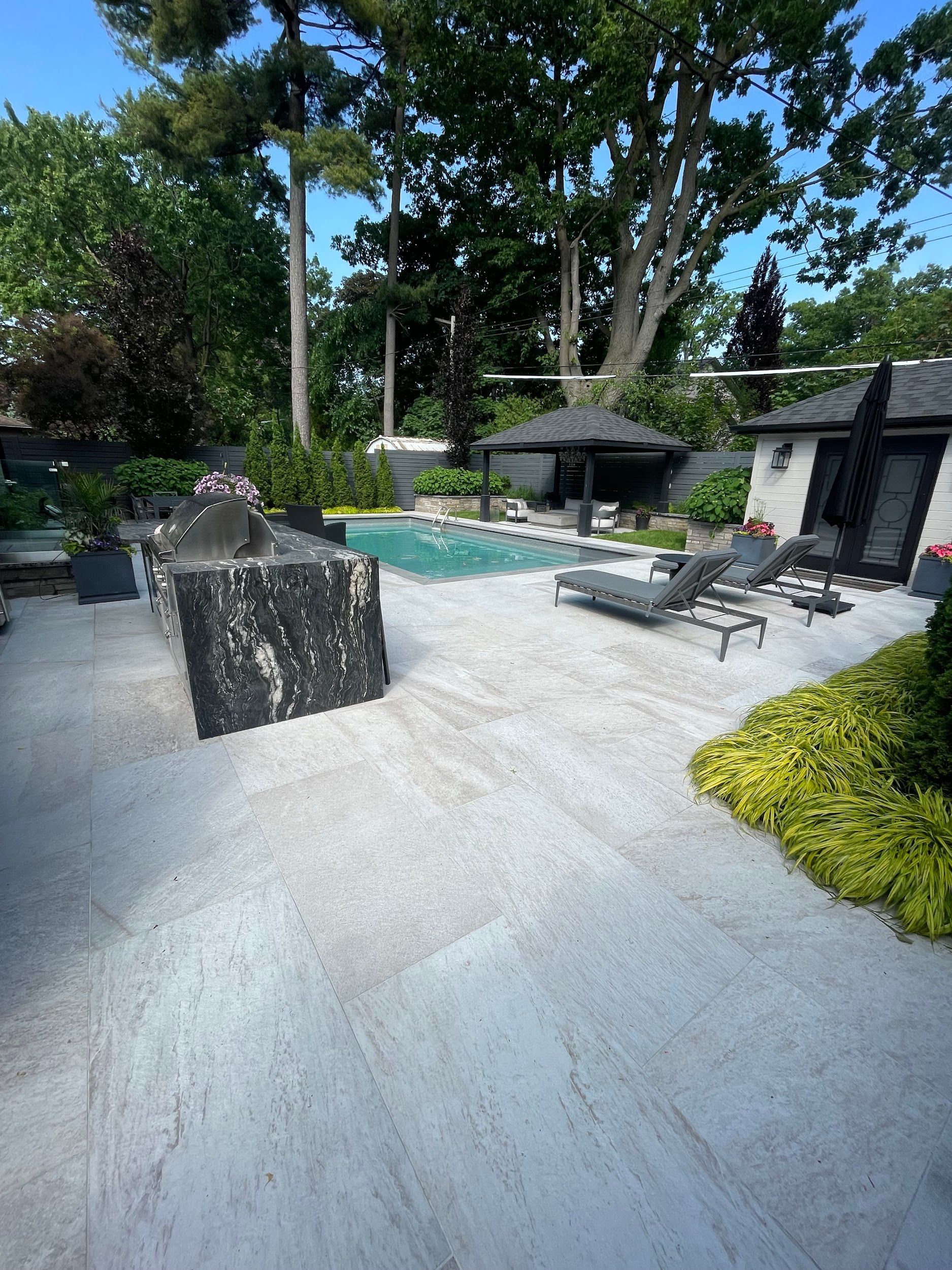 Backyard patio with pool, outdoor kitchen, lounge chairs, and a small structure.