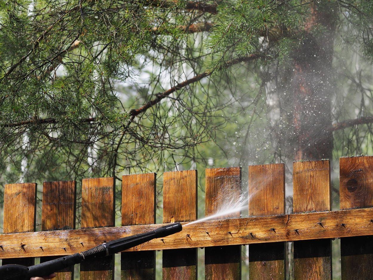 Pressure washing a wooden fence, water spraying, outdoors.