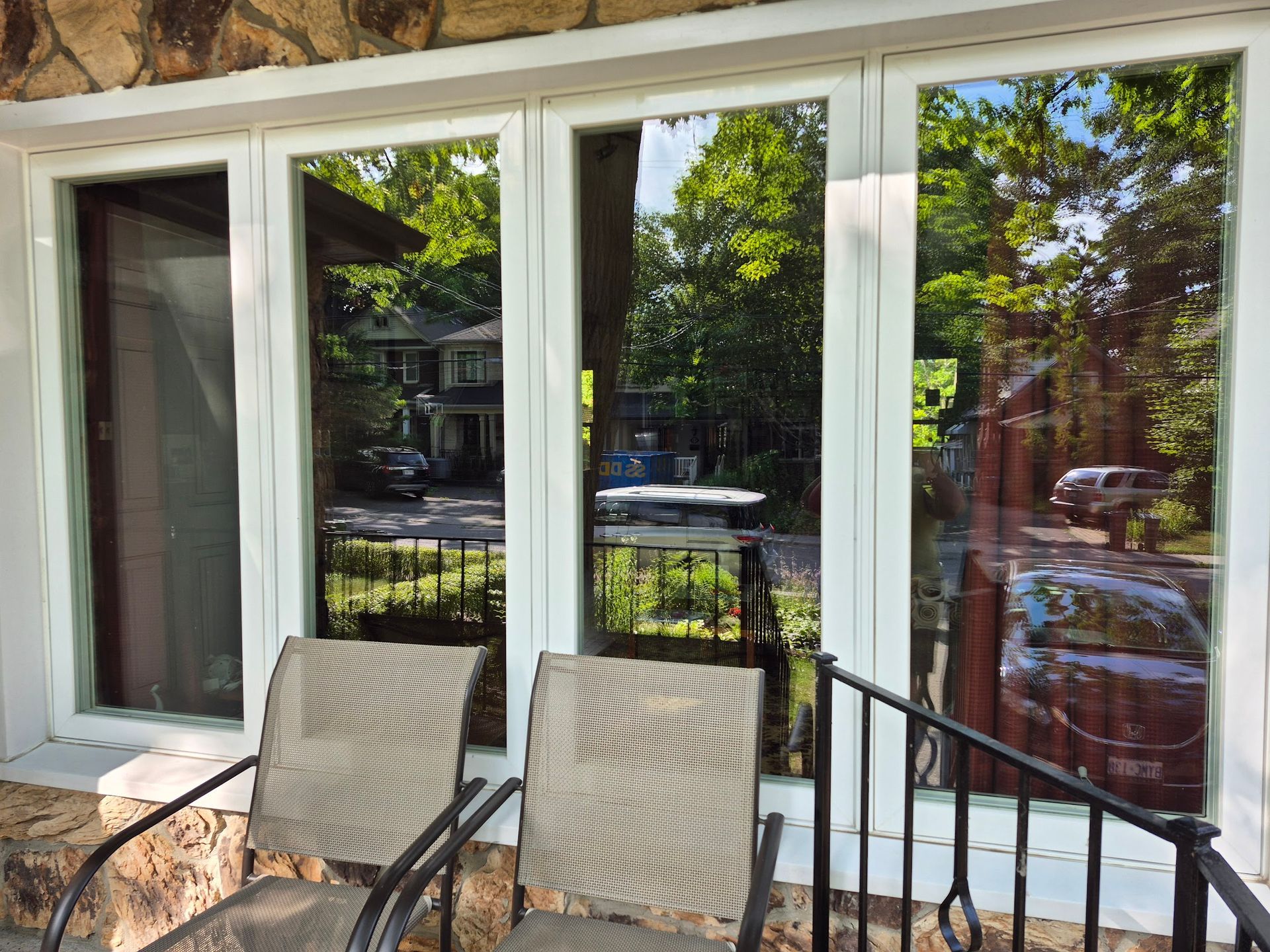 Chairs on a porch with reflective windows showing a street and trees, framed by white trim.