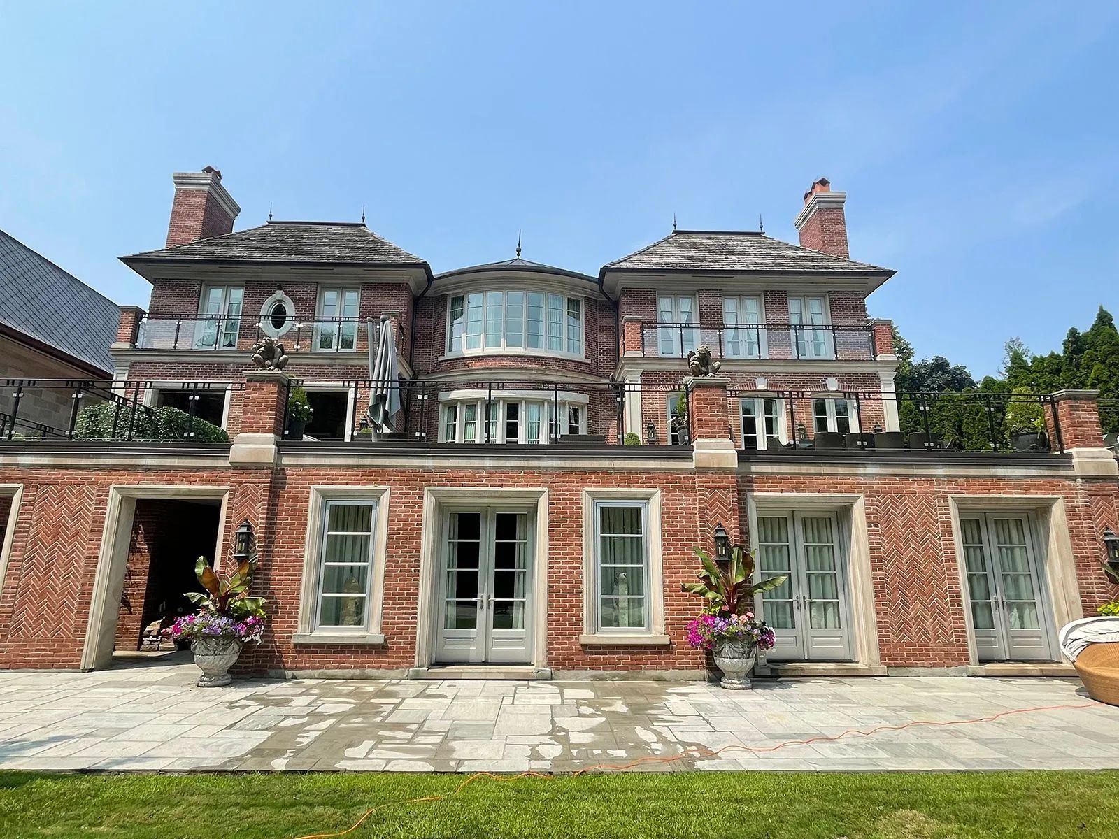 Large red brick house with multiple stories, windows, and balconies under a blue sky.