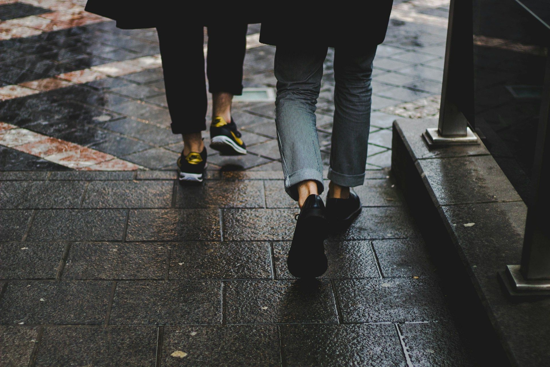 Two people are walking down a wet sidewalk on a rainy day.