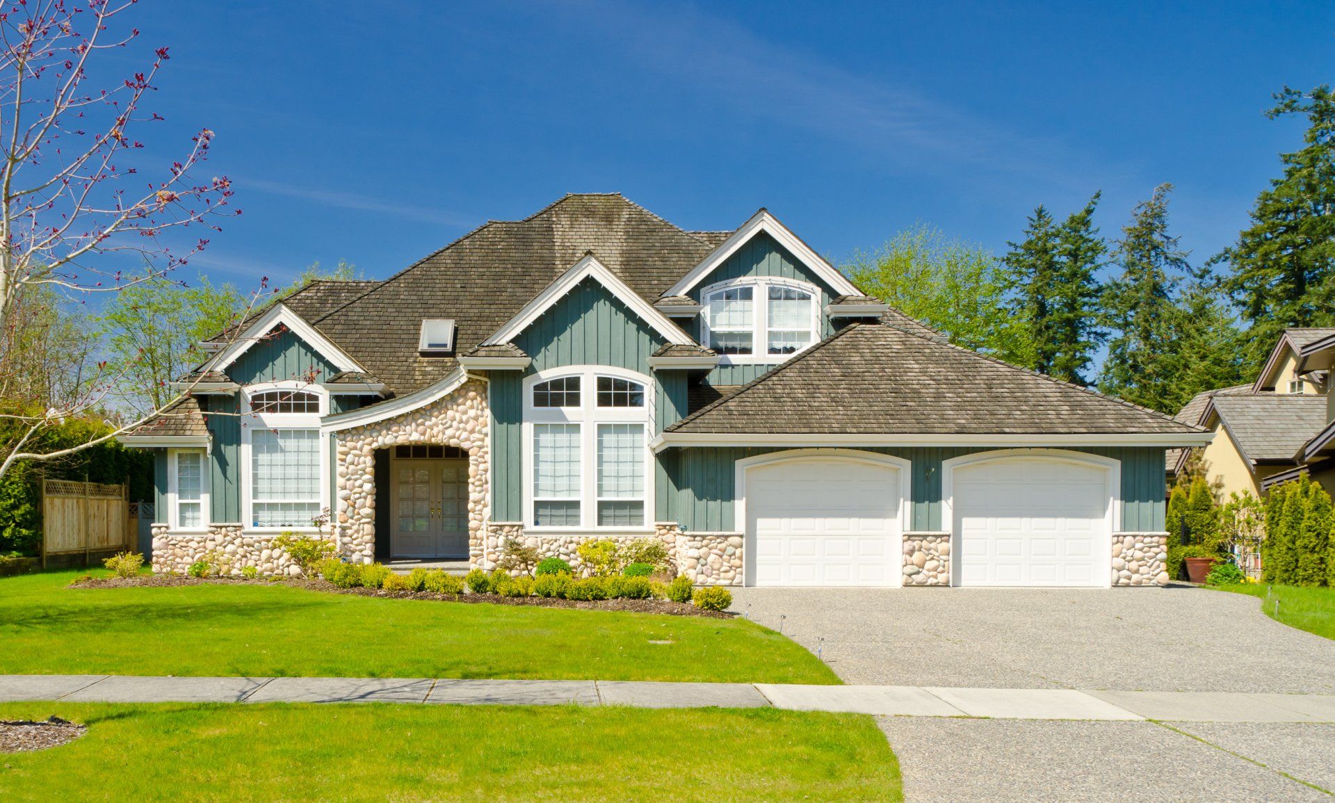 Suburban house with stone facade, white garage, and manicured lawn under a clear blue sky
