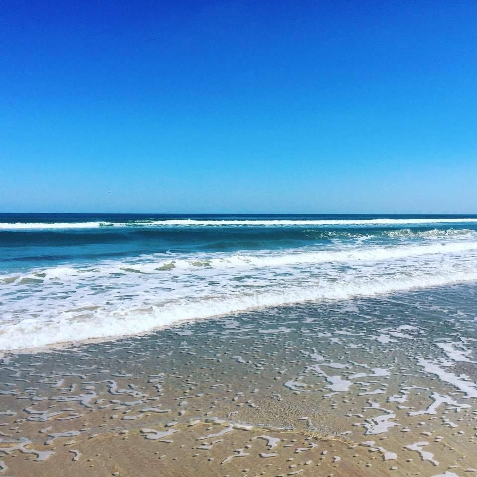 Sandy beach with foamy waves under a bright blue sky