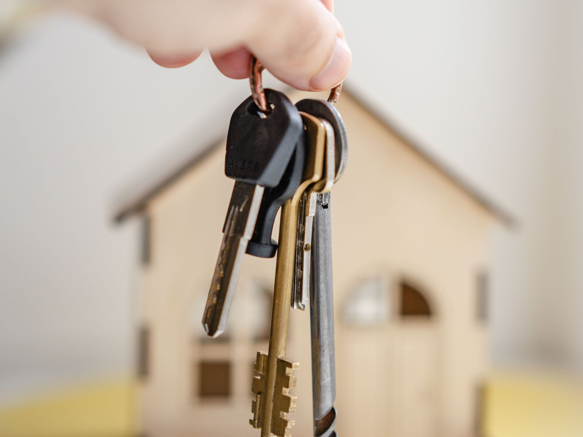 Hand holding a set of keys in front of a small wooden house model