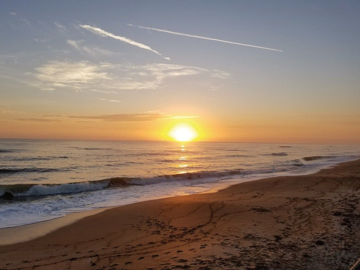 Sunset over a calm ocean with gentle waves and a sandy beach