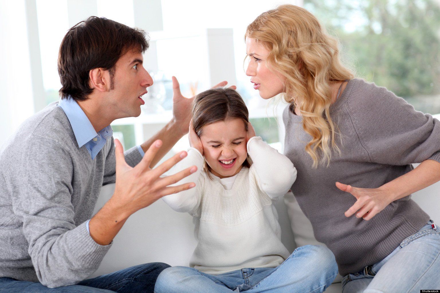 A man and woman are sitting on a couch yelling at a little girl who is covering her ears.