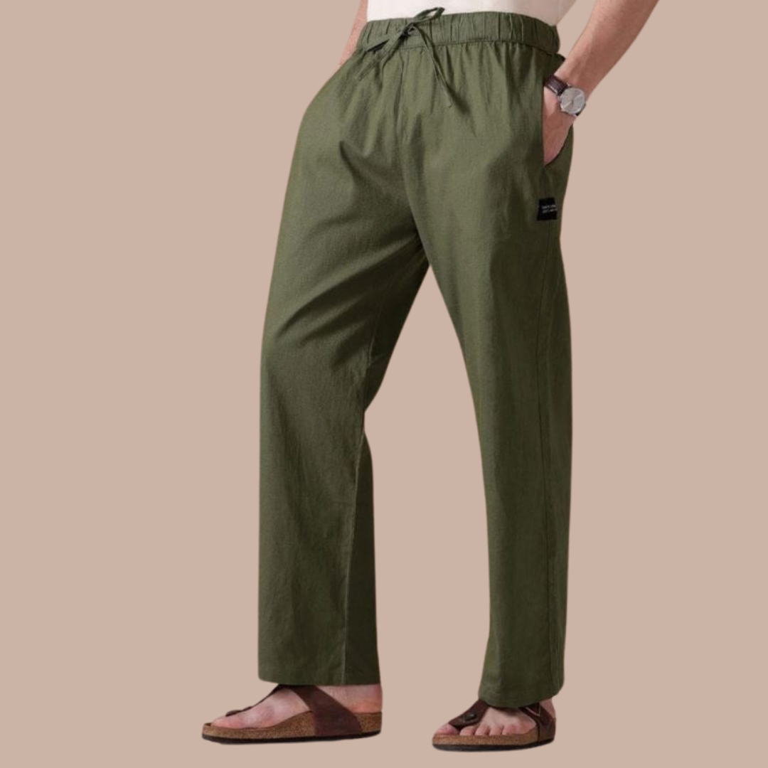 A man wearing a white shirt and green pants is standing with his hands in his pockets.