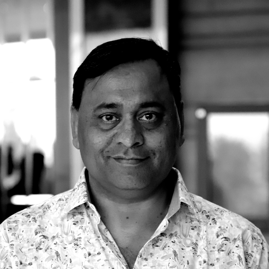 A man in a floral shirt is smiling in a black and white photo.