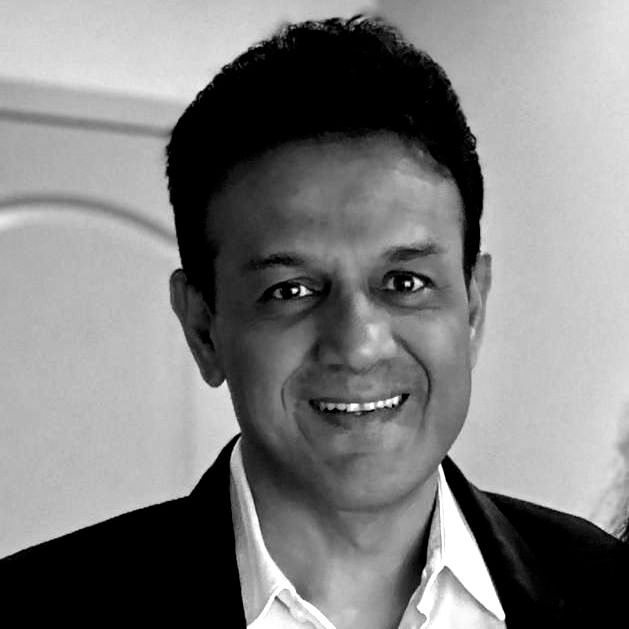 A man in a suit and white shirt is smiling in a black and white photo