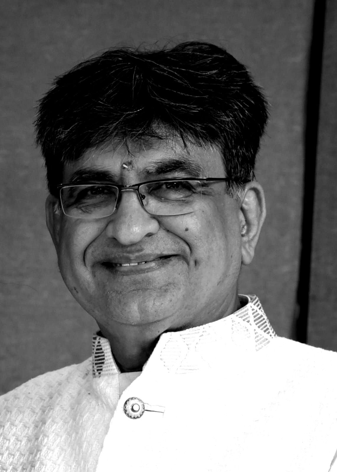 A man wearing glasses and a white jacket is smiling in a black and white photo.