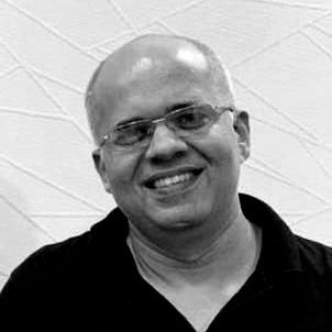 A man wearing glasses and a black shirt is smiling in a black and white photo.
