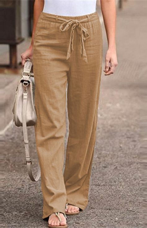 A woman wearing a white shirt and brown pants is walking down the street.