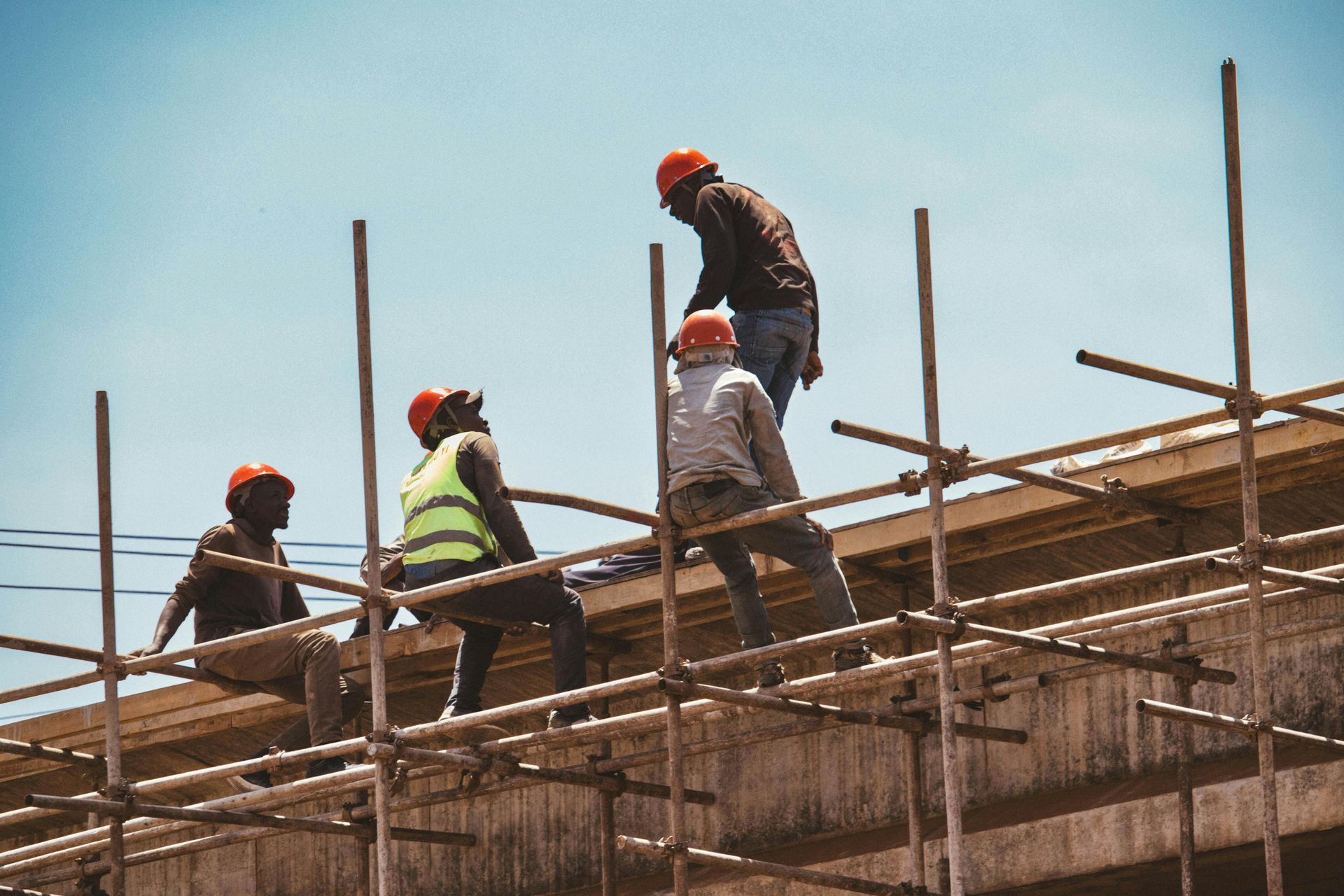 Construction workers on scaffolding, under a blue sky. One worker wearing a safety vest.
