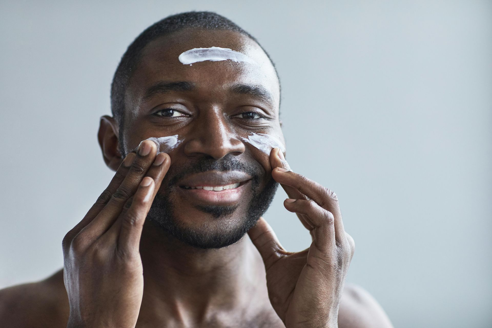 A man is smiling while applying cream to his face.