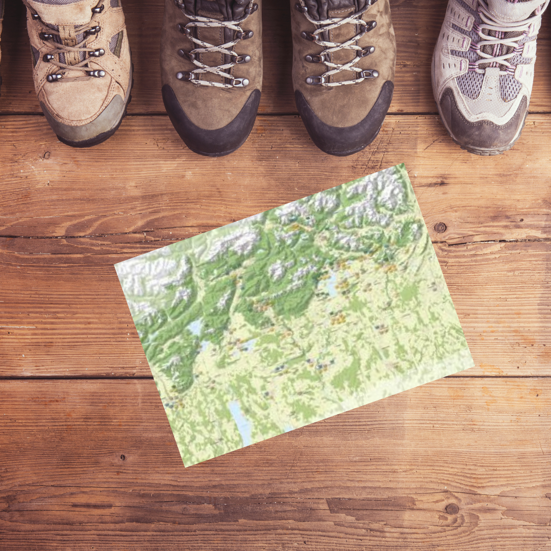Drei Paar Wanderschuhe stehen neben einer Karte auf einem Holztisch.
