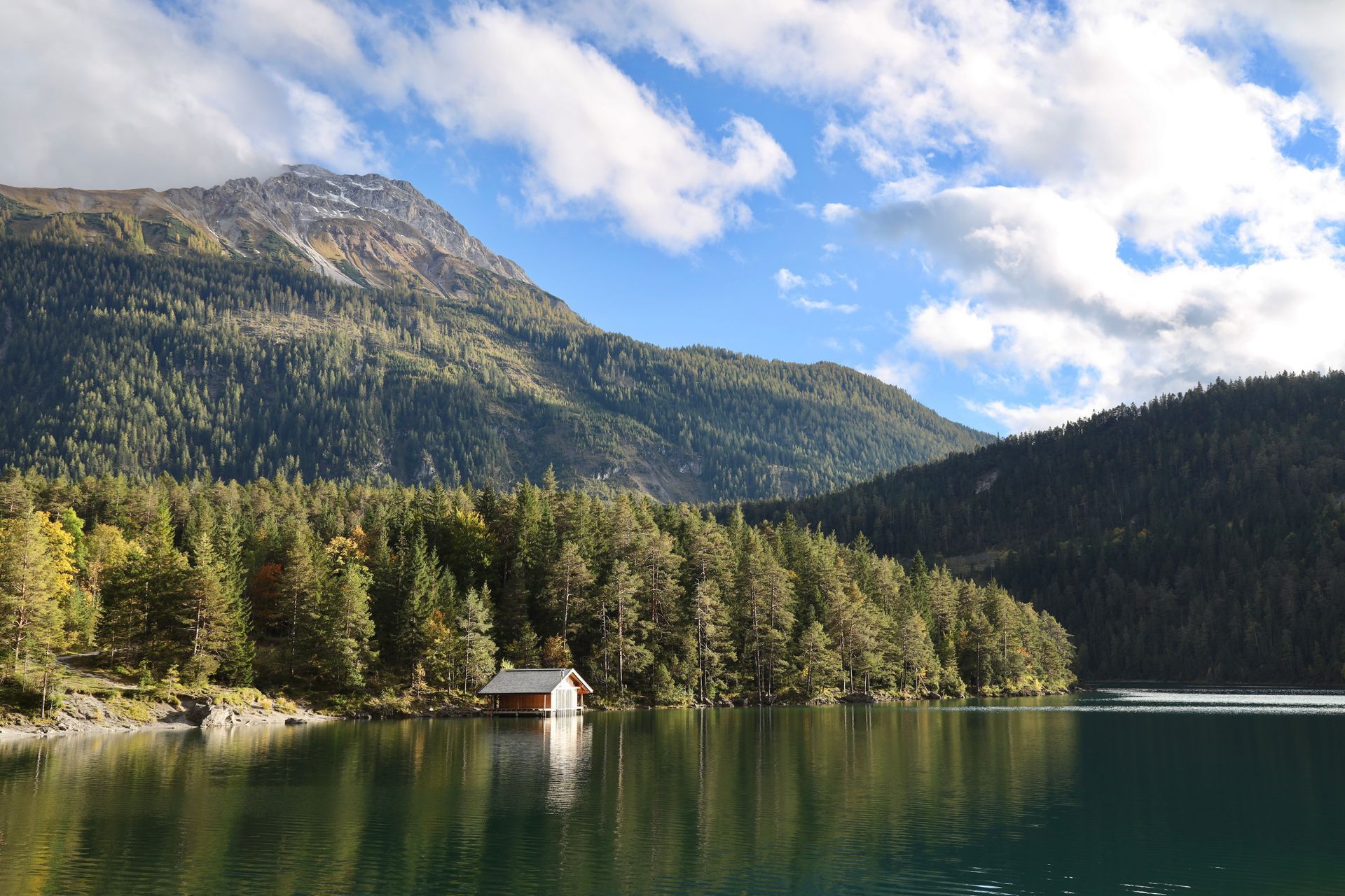 Ein kleines Haus liegt am Ufer eines Sees mit Bergen im Hintergrund