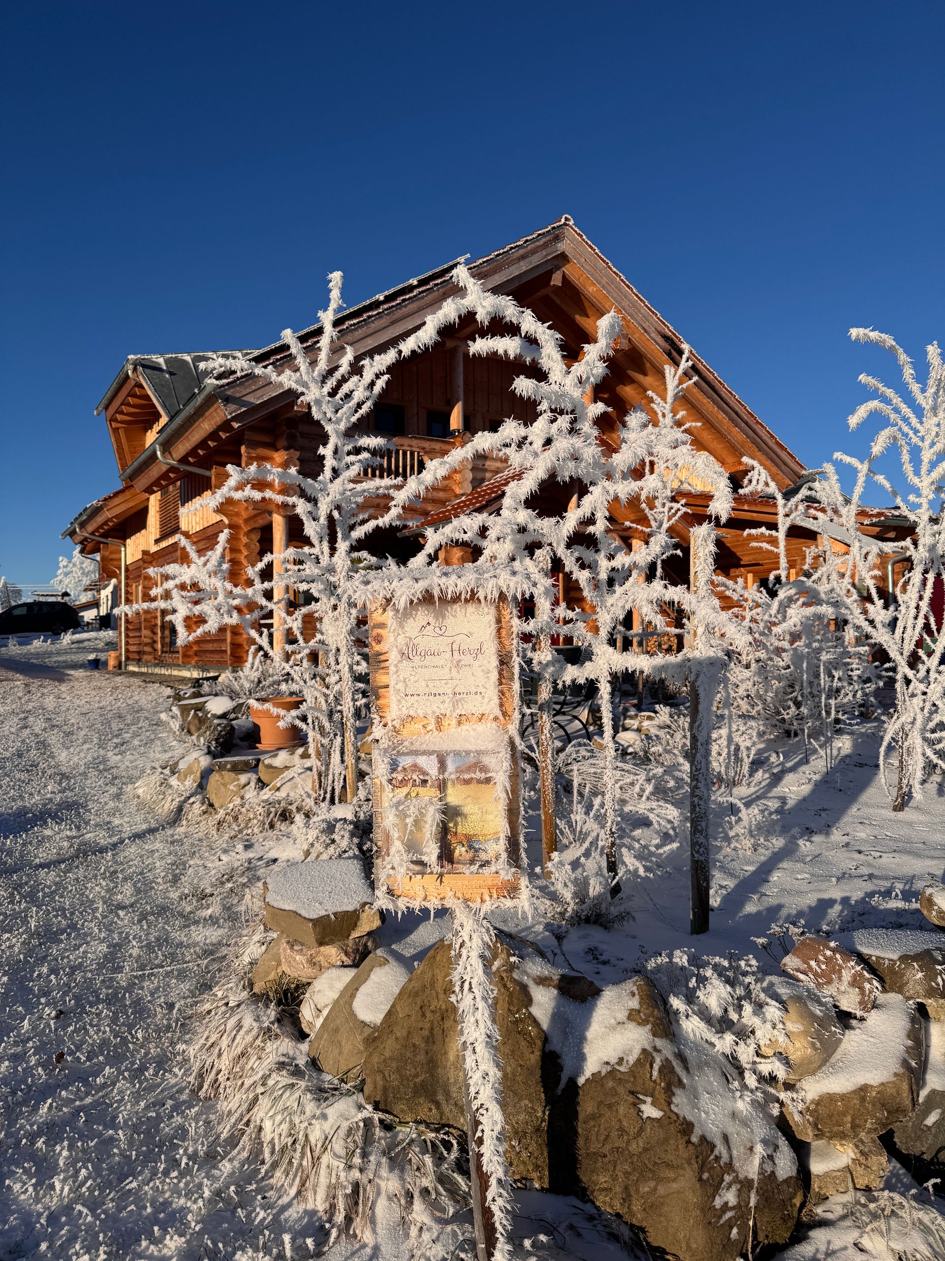 Verschneite Blockhütte mit frostbedeckten Bäumen und klarem, blauem Himmel.