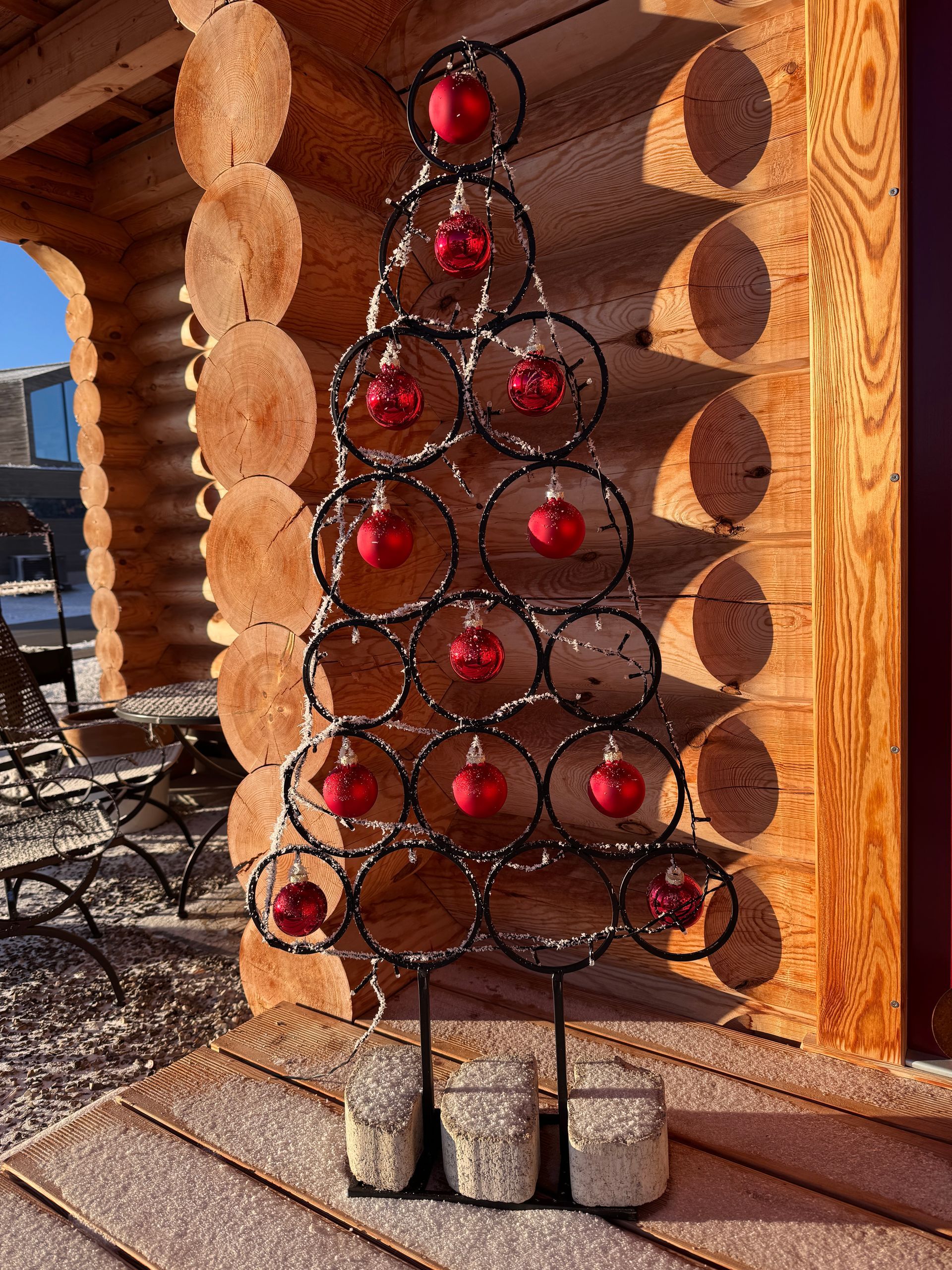 Christbaumschmuck aus Metall mit roten Ornamenten vor einer Holzhüttenwand.