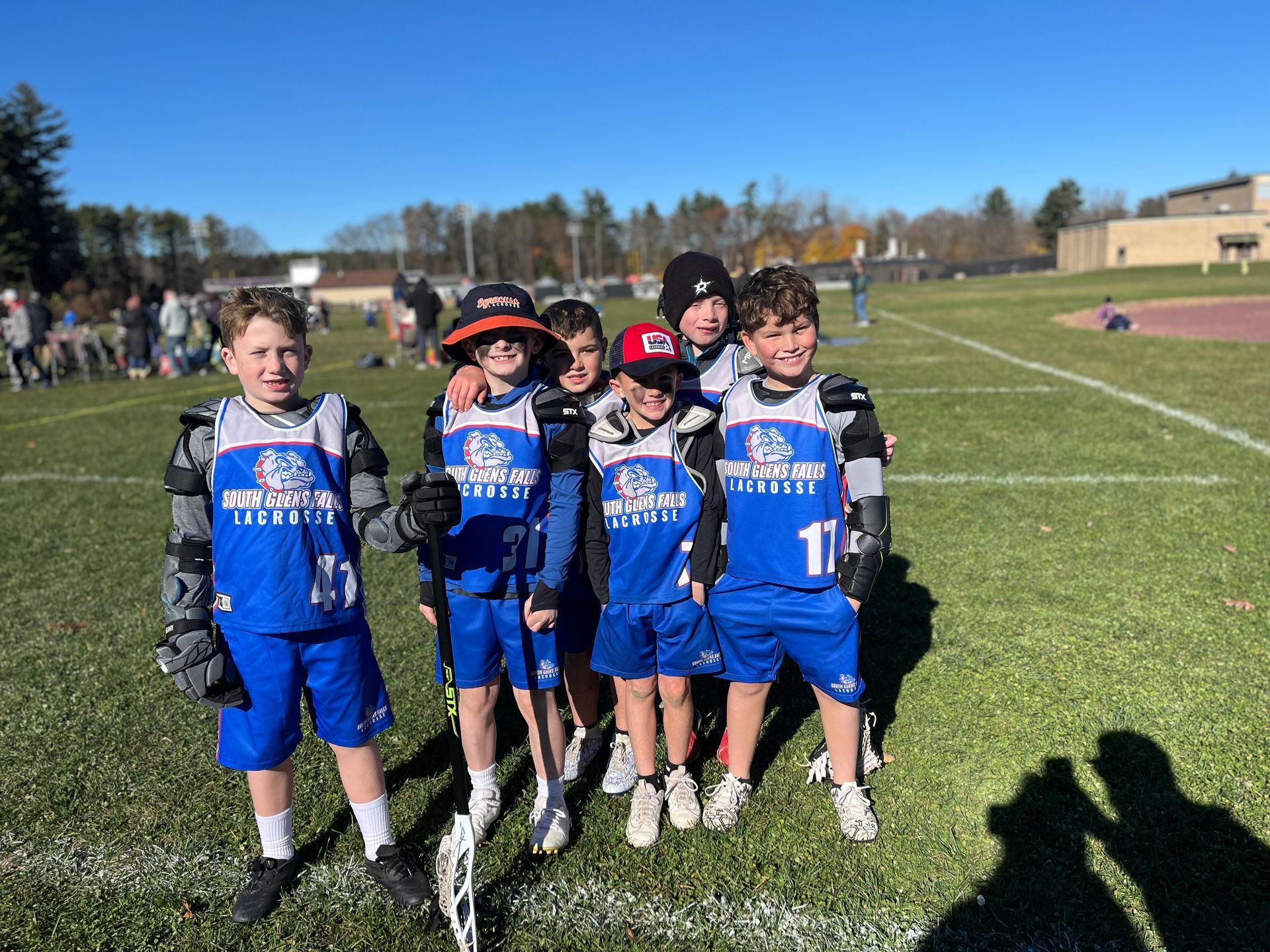 Youth lacrosse team, in blue uniforms, posing on a sunny field.