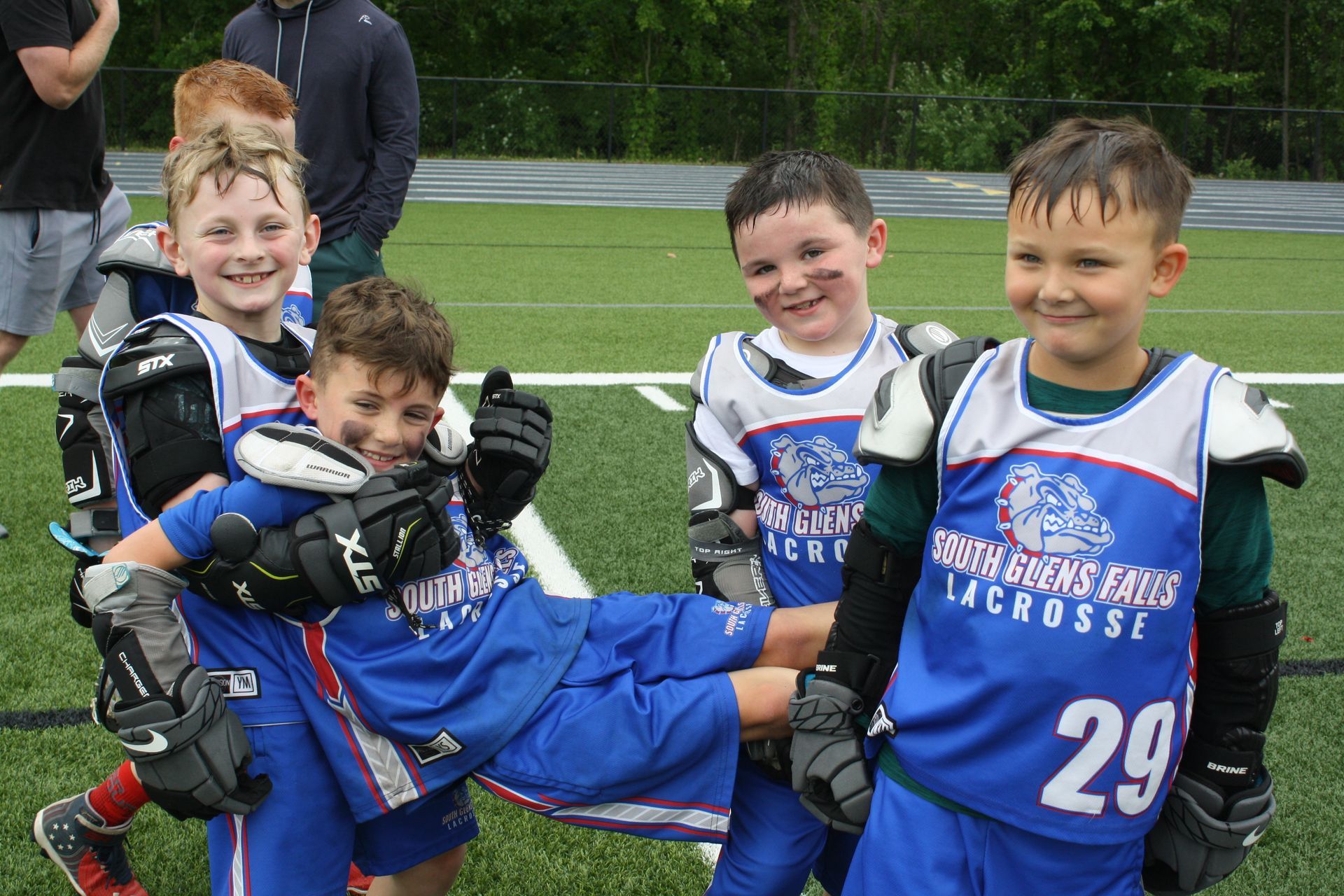 Youth lacrosse players in blue uniforms, celebrating on a green field.