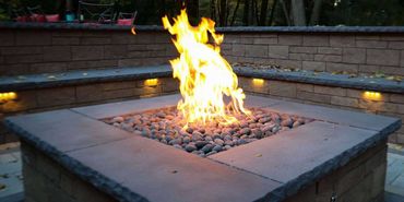 A lit fire in a stone fire pit, surrounded by stone seating and a brick wall.